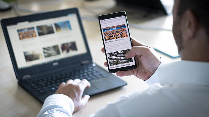 Person sitting in front of a laptop holding a mobile phone